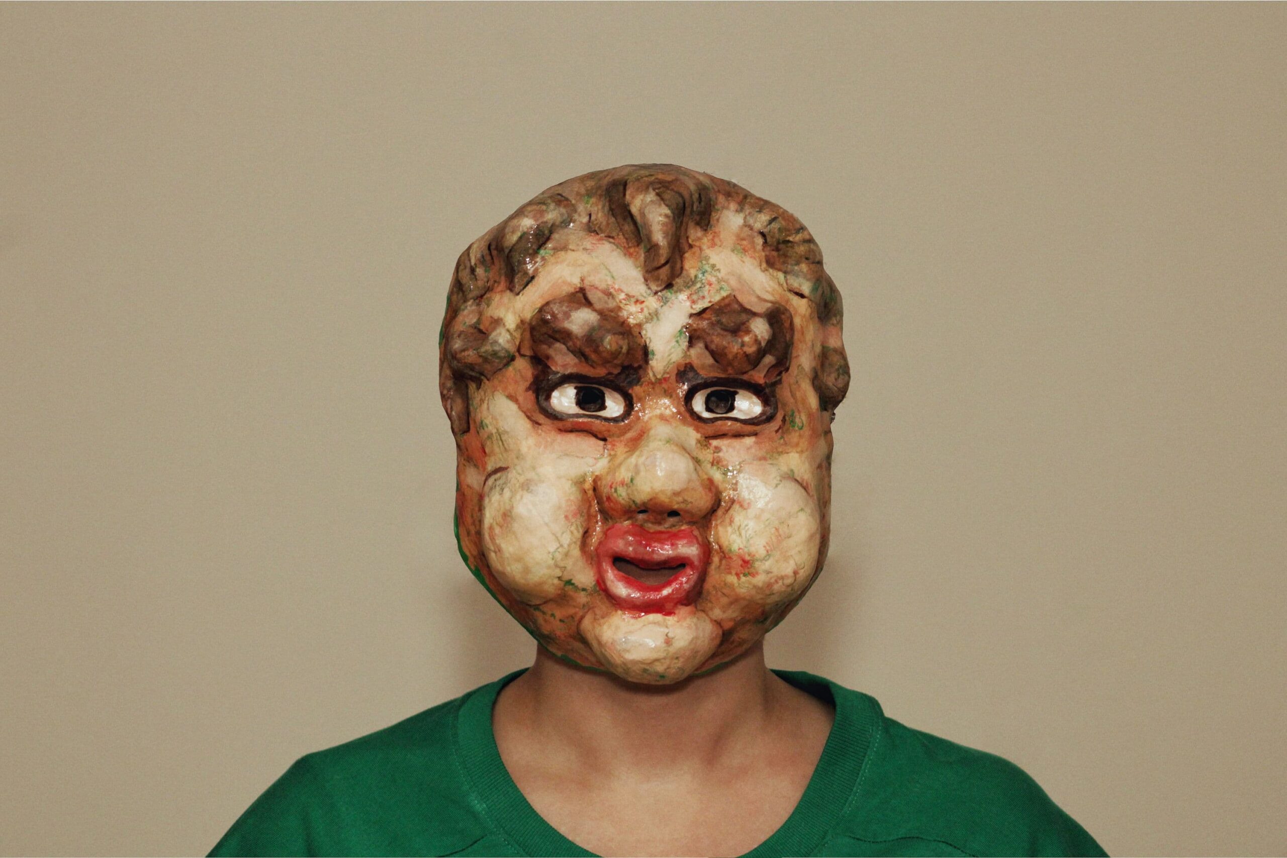 handmade expressive mask with exaggerated facial features and slicked curls, worn over a human face