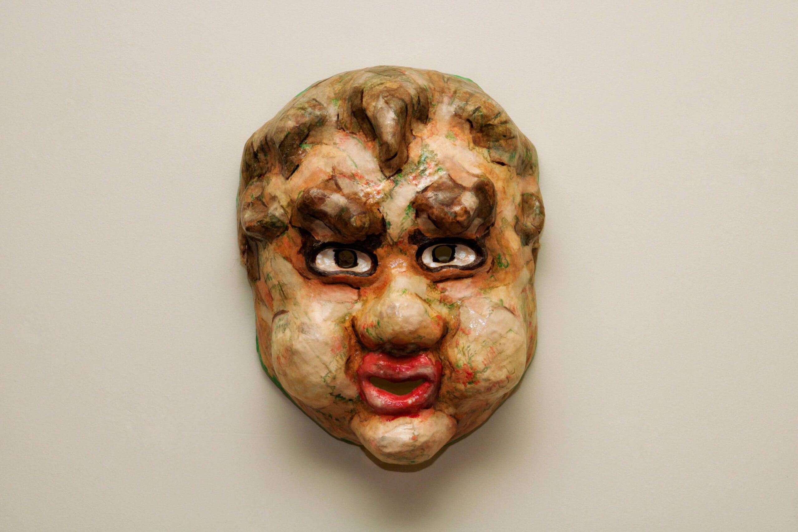 mounted mask with cartoon-like features and dense surface markings, evoking a caricatured male face