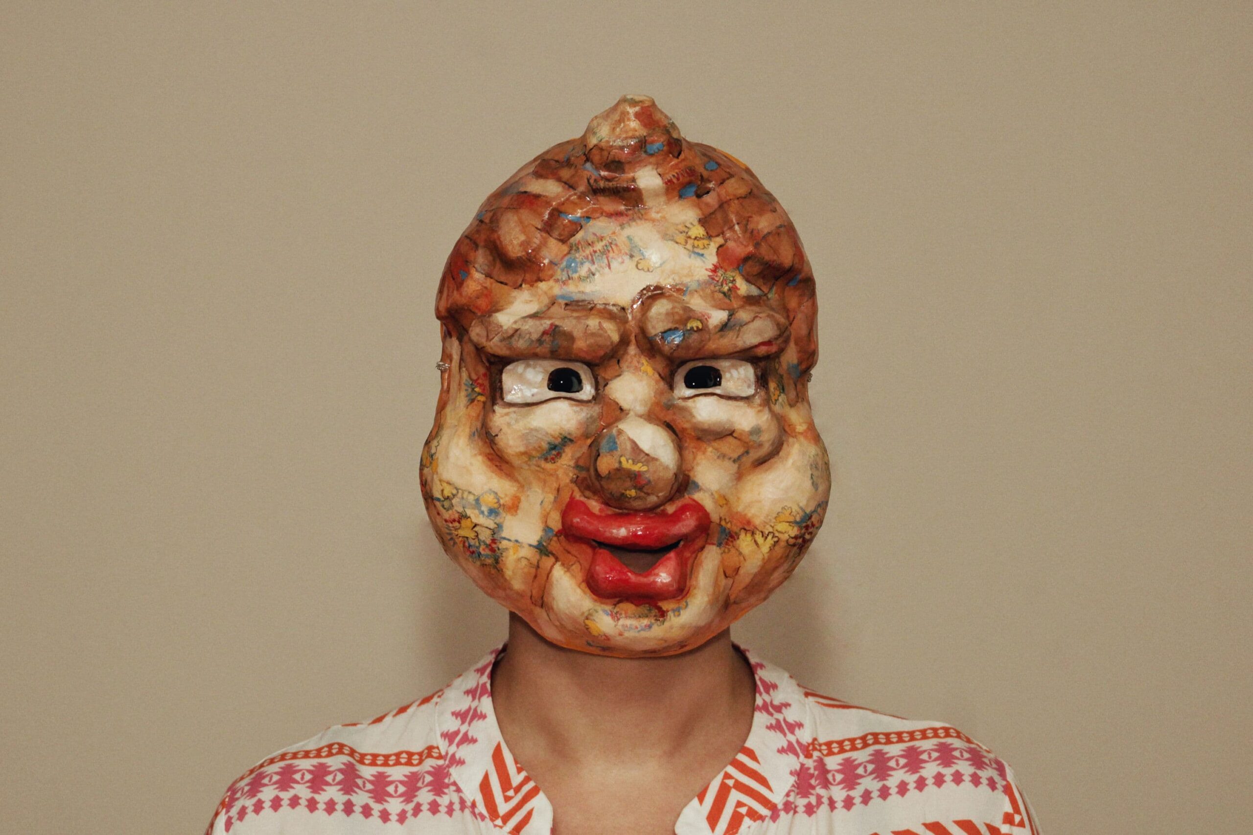 oversized cartoonish mask with bloated features and leathery hair, evoking a lost animation character