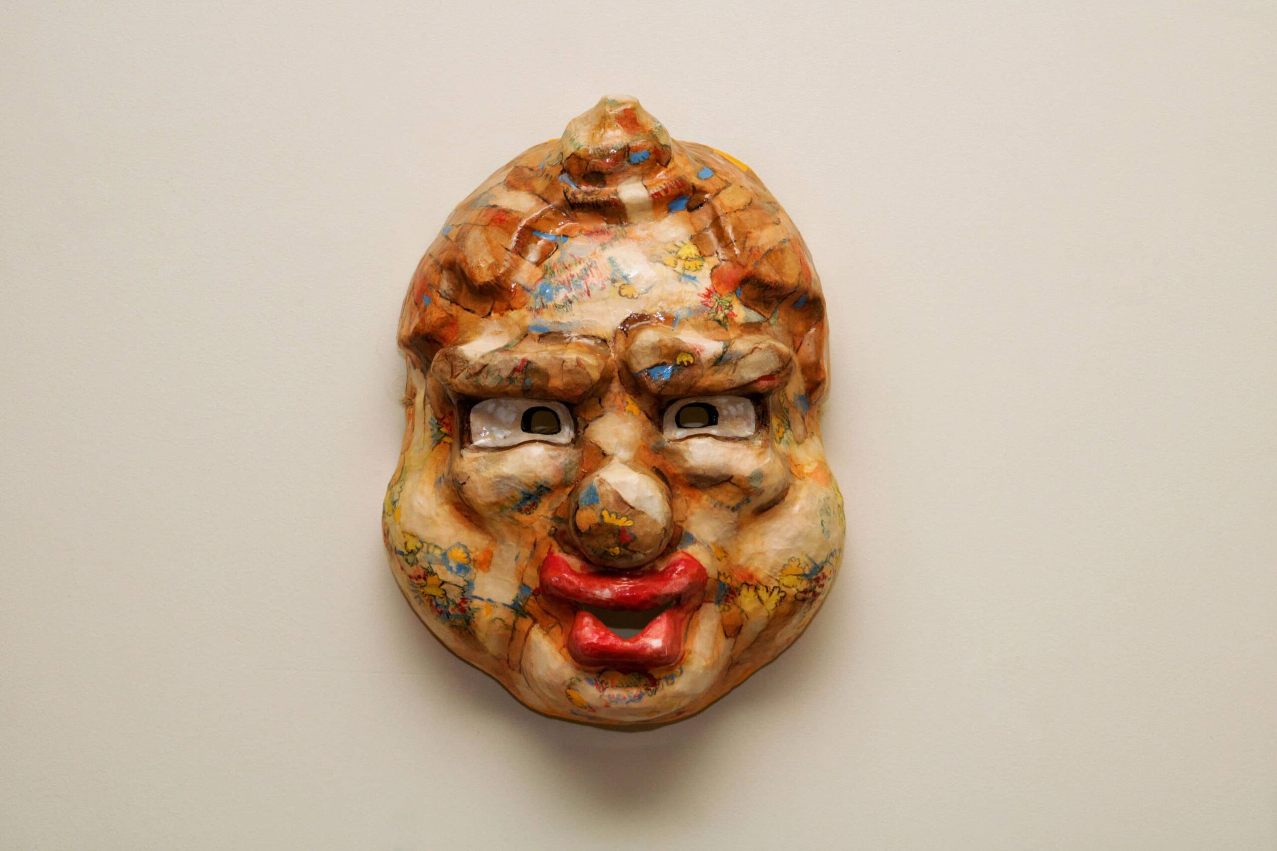 wall-mounted caricature mask, blending cartoon absurdity with aged faux-leather skin