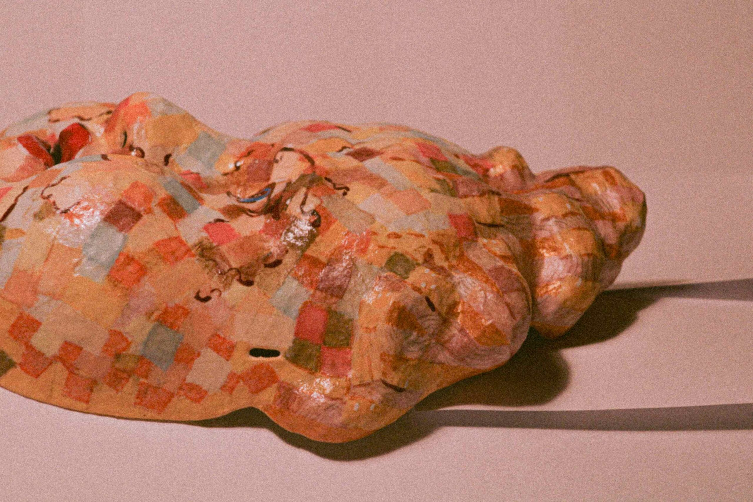 side view of the sculpted face resting horizontally, highlighting the cheek, hair and uneven, mosaic-like surface