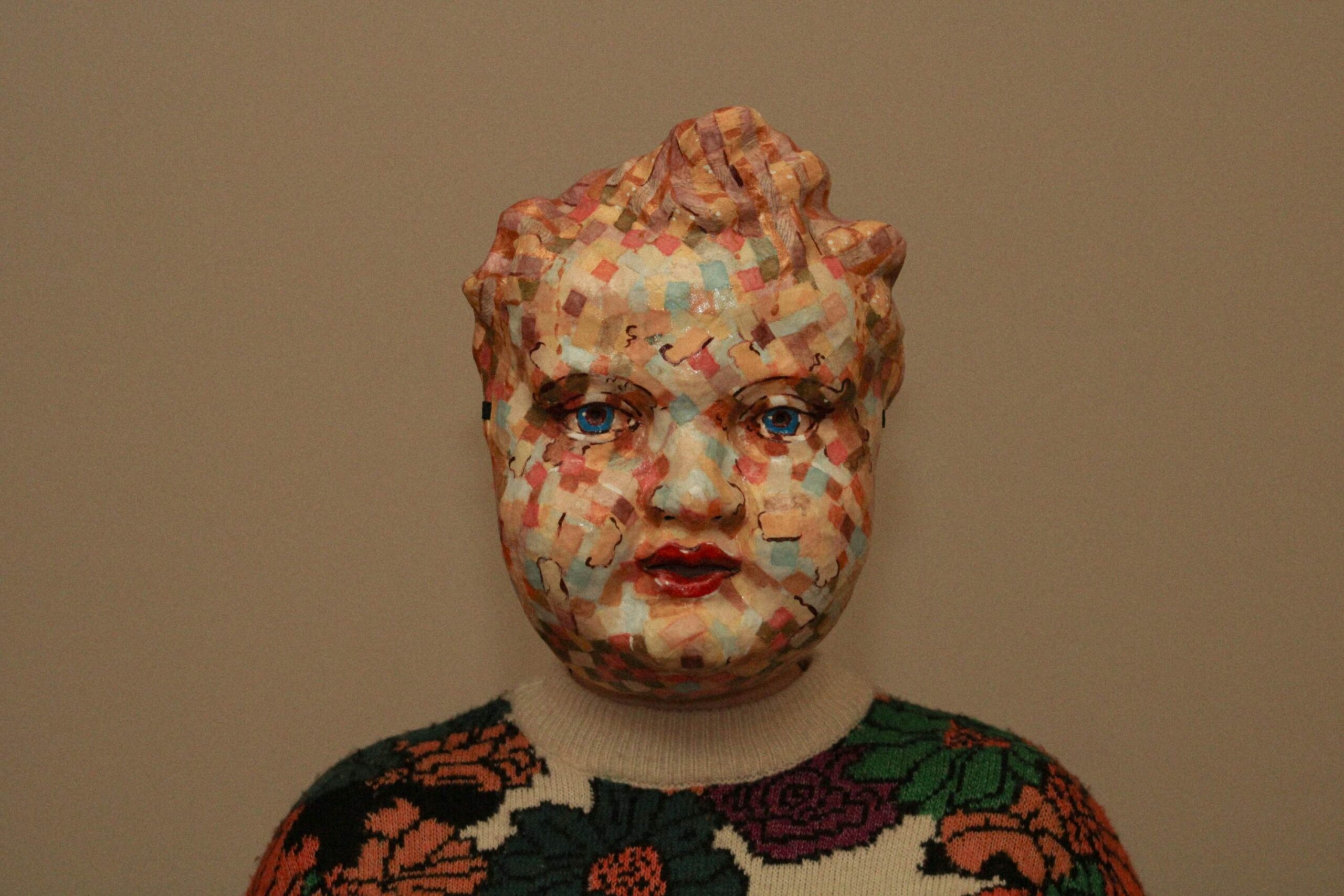 medium shot of a person wearing the sculpted mask, centered against a plain background