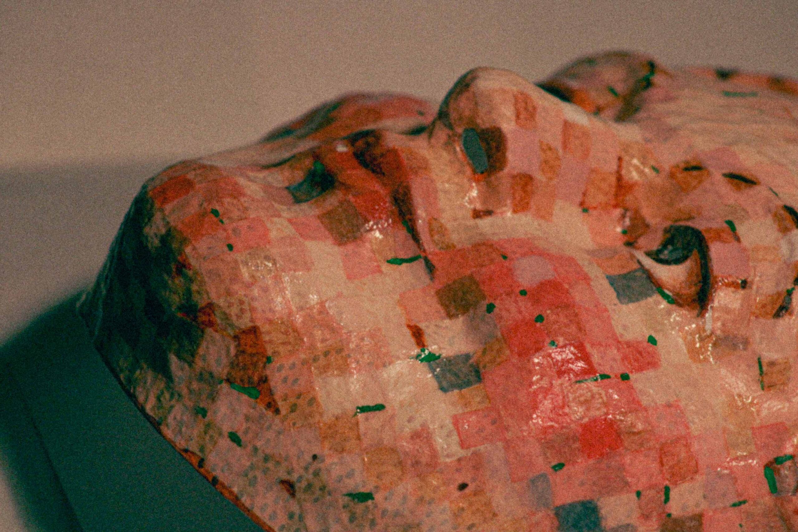 angled close-up of the sculpted face, highlighting the cheek, eye socket, and layered patchwork pattern with visible brushstrokes