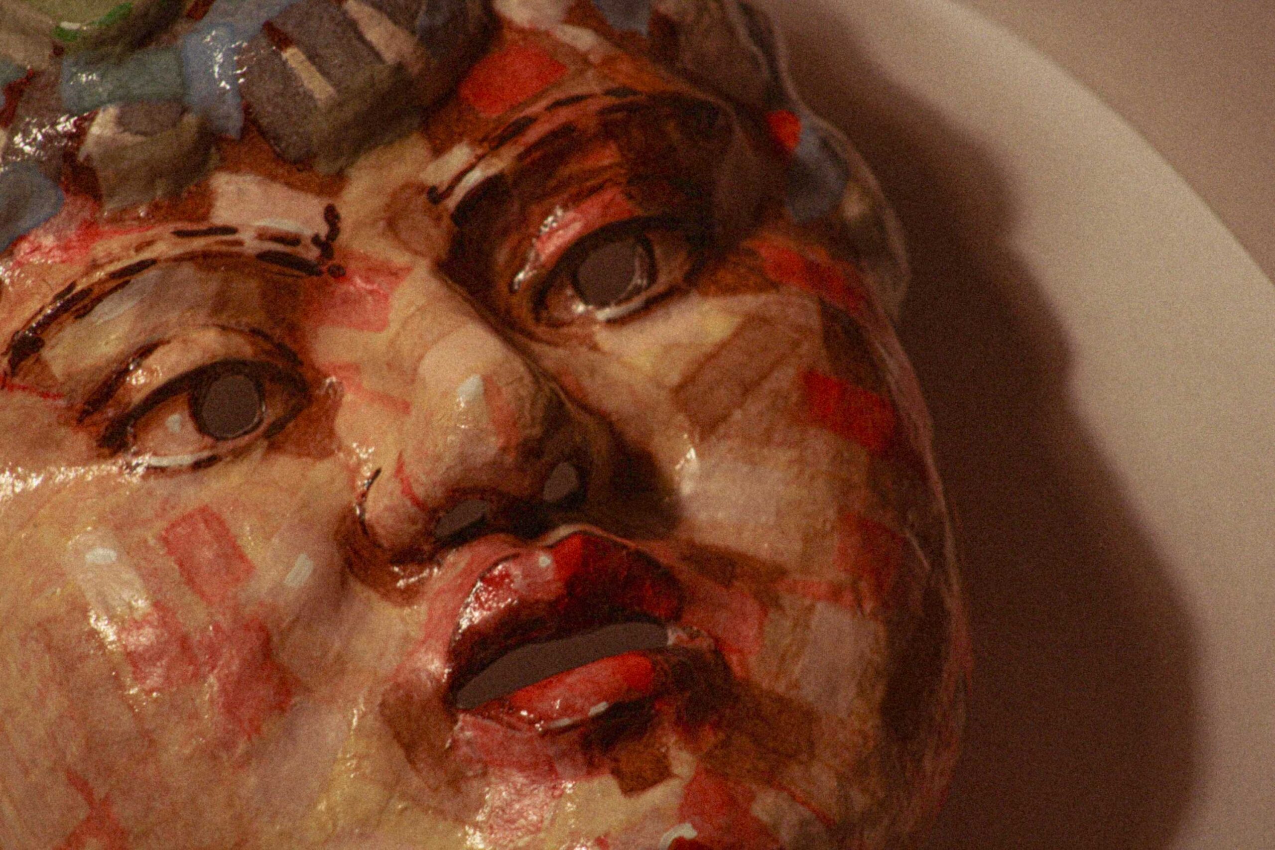 close-up of a sculpted face lying on its side, showing the eyes, nose, and parted lips covered in patchwork of red, beige and brown painted rectangles