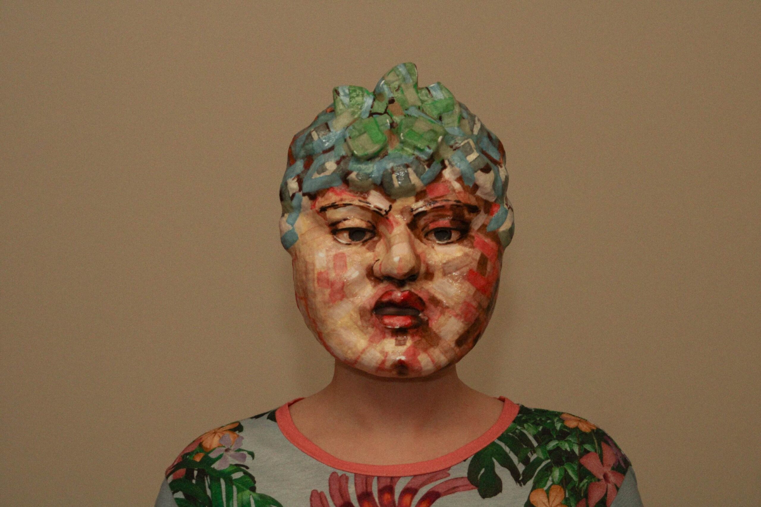 medium shot of a person wearing the sculpted mask, centered against a plain background