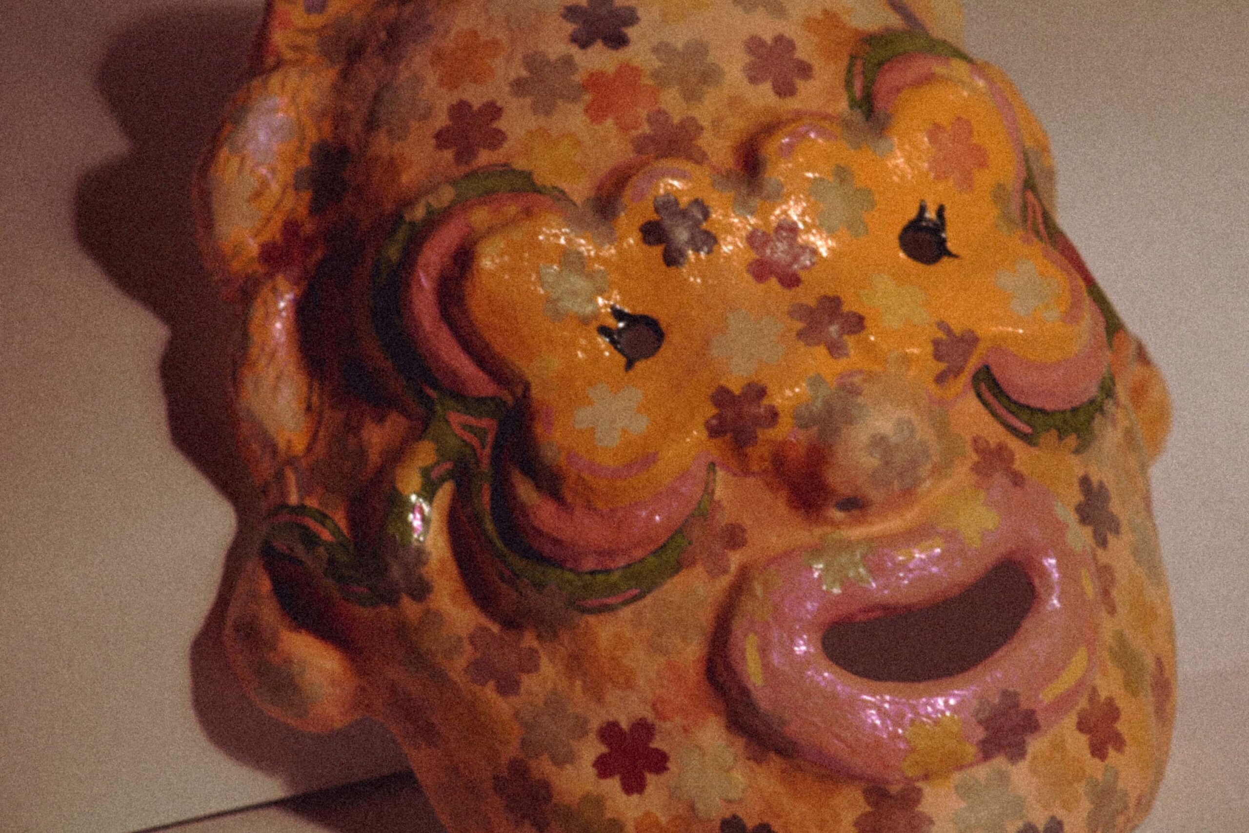three-quarter view of a colorful handmade sculptural mask with open mouth and detailed floral decoration