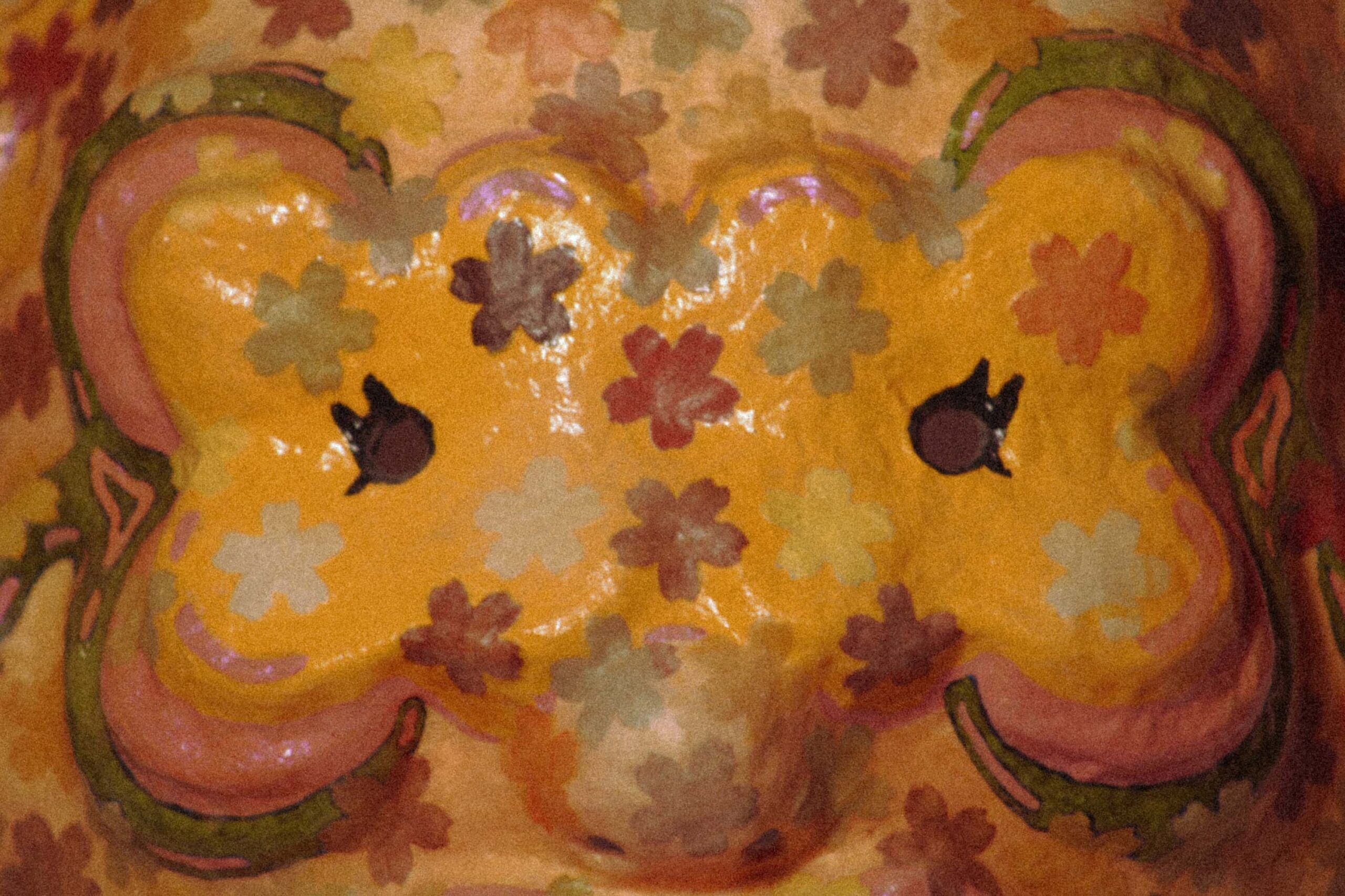close-up of a handmade sculptural mask with floral pattern, showing eye holes and glossy painted surface