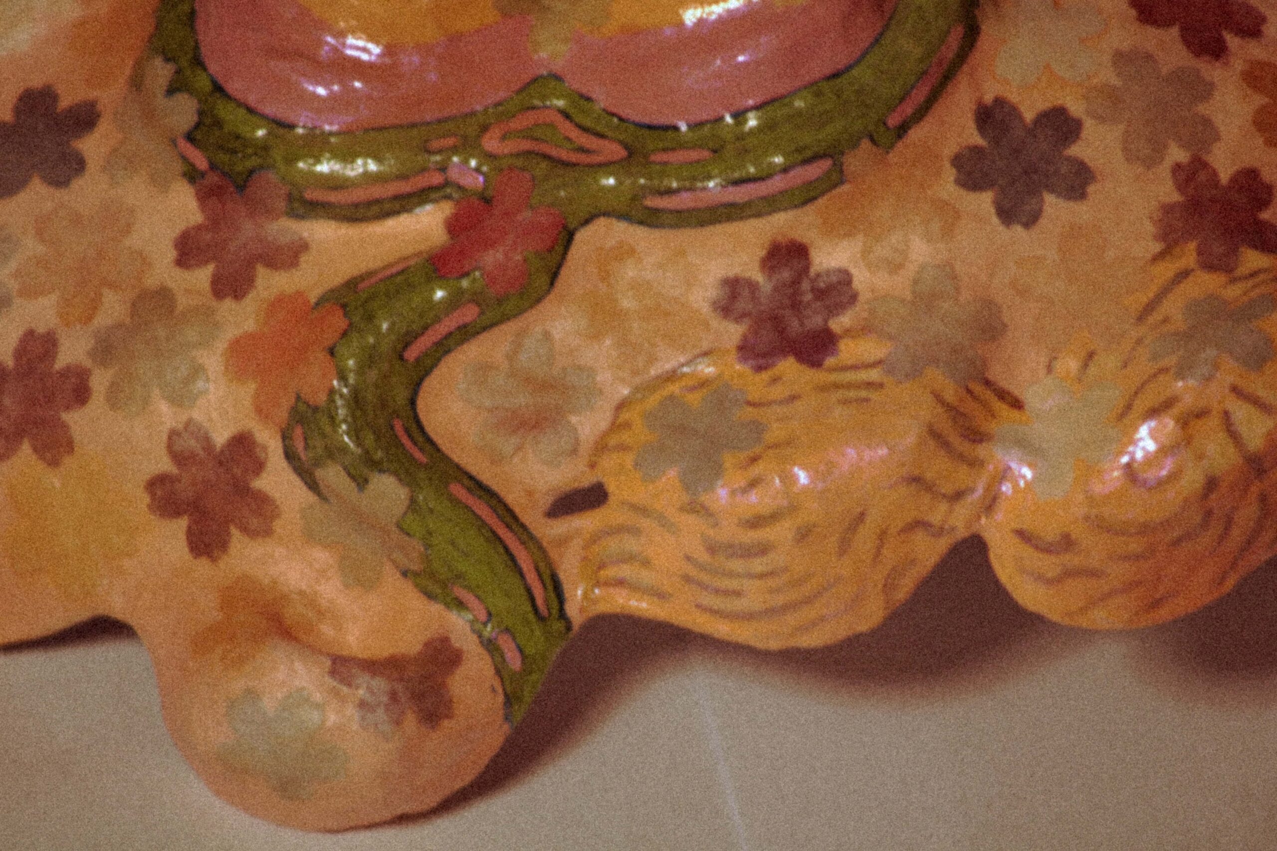 close-up detail of a handmade mask with green lines and small multicolored floral patterns on textured surface