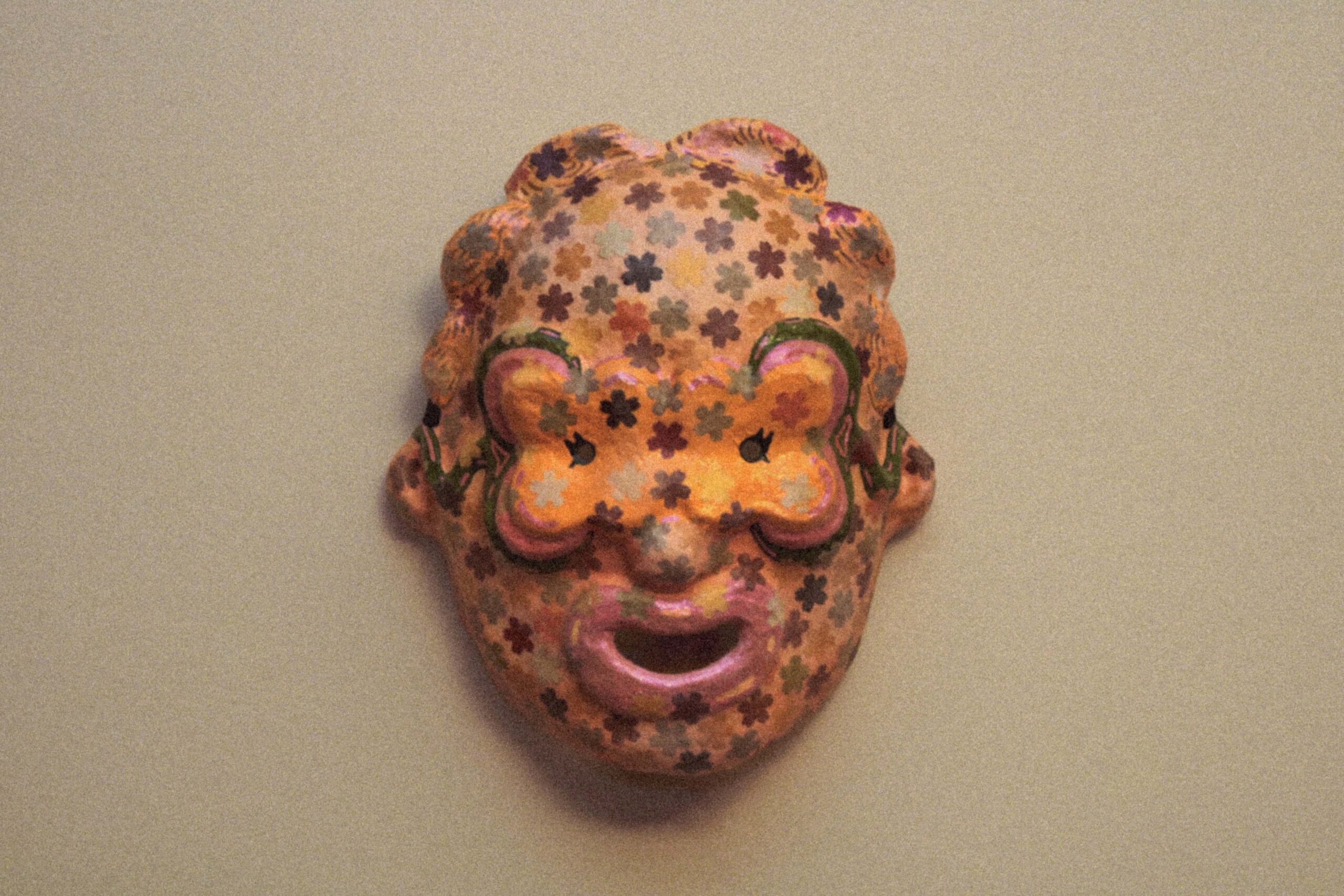 front view of a handmade sculptural mask against plain background, showing symmetrical shape and bright decoration
