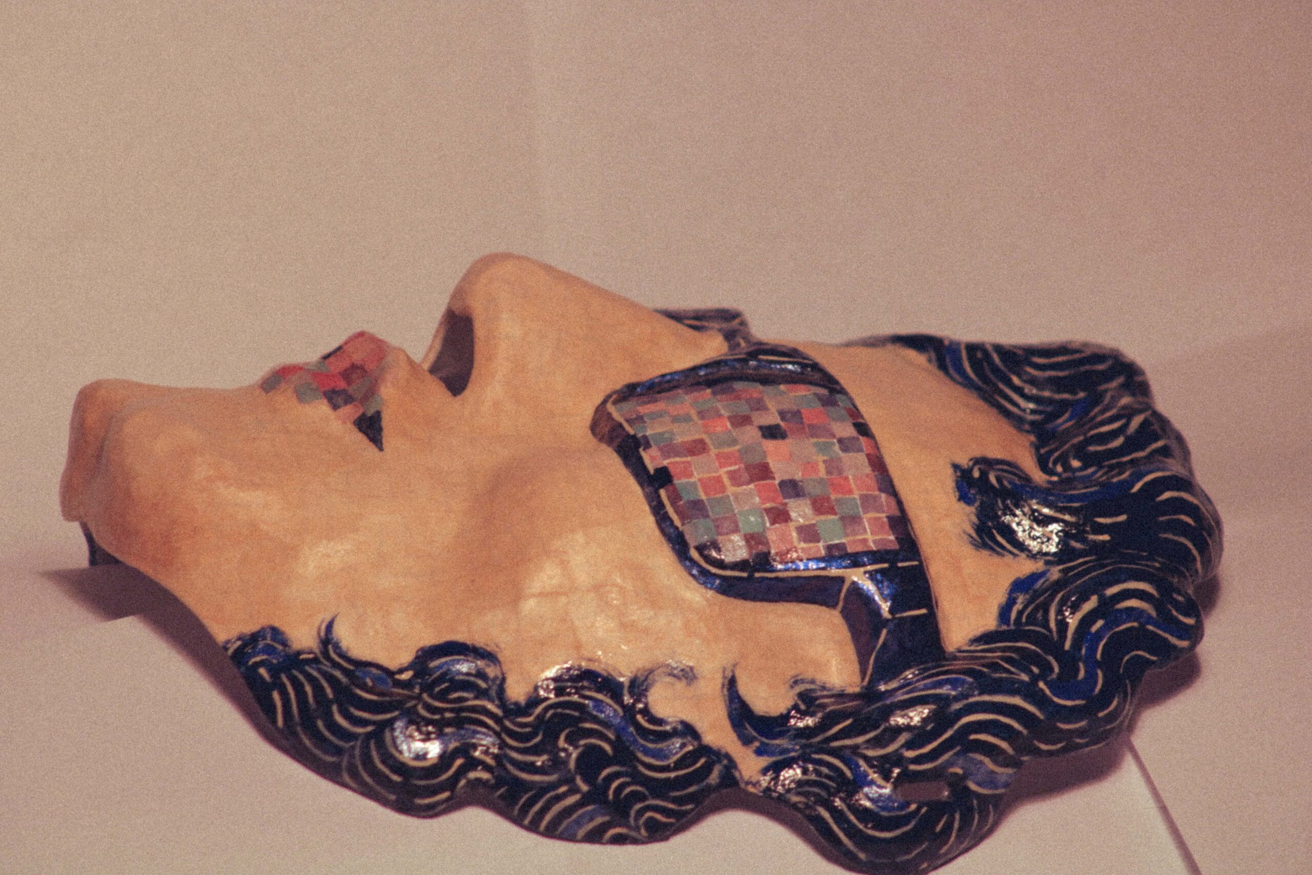 side view of a handmade sculptural mask with painted sunglasses, curly hair details, and glossy textured surface