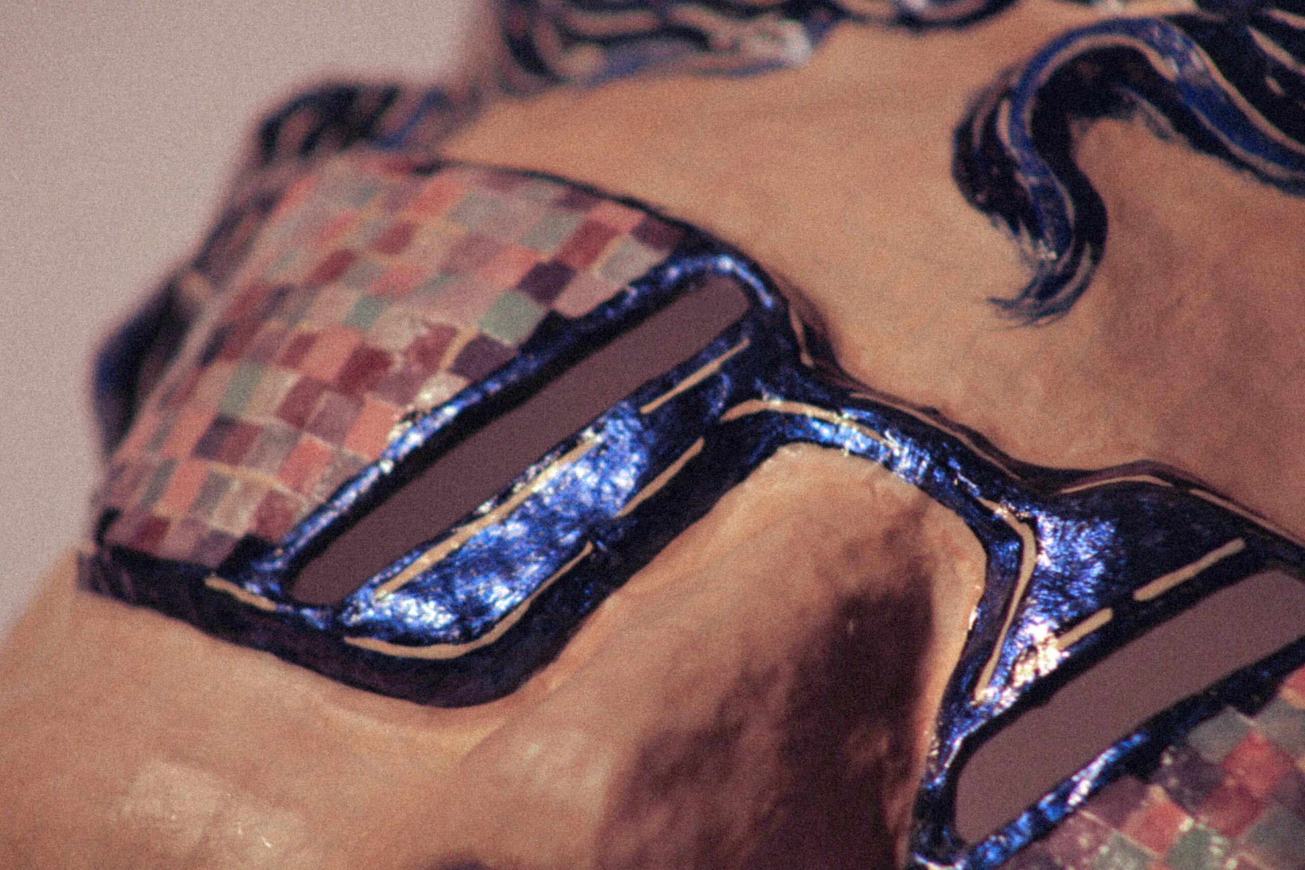 extreme close-up of a sculptural mask with blue-framed sunglasses and multicolored mosaic pattern on lenses