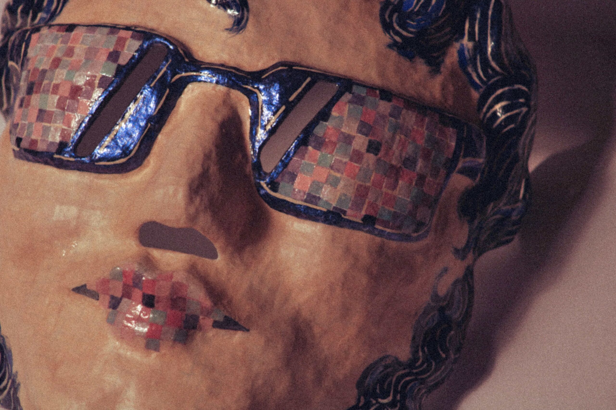 detailed close-up of a sculptural mask face with sunglasses and textured painted surface