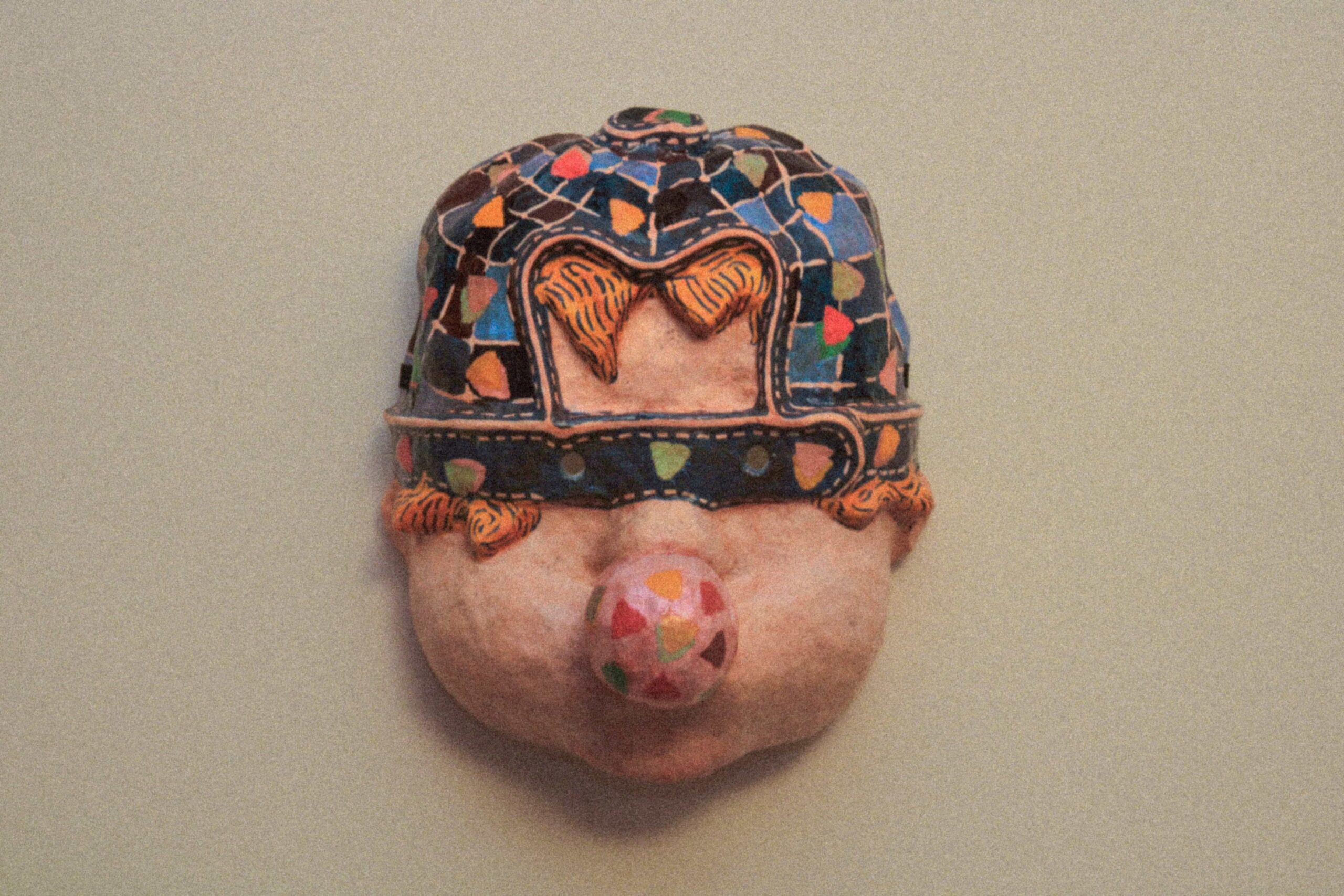 front view of a handmade contemporary art mask with mosaic surface and exaggerated nose, mounted on wall